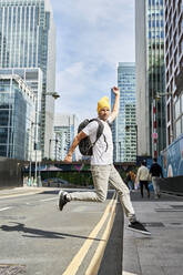 Mann mit Strickmütze springt auf der Straße vor einem Gebäude - VEGF05999