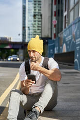 Nachdenklicher Mann mit Smartphone auf dem Fußweg sitzend - VEGF06000