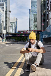 Mann mit Smartphone auf dem Gehweg in der Stadt sitzend - VEGF06001