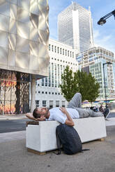 Man relaxing on bench in front of buildings - VEGF06008