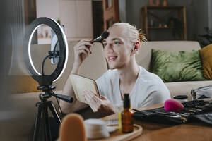 Lächelnde Influencerin, die zu Hause ein Make-up-Tutorial per Smartphone filmt - YTF00189