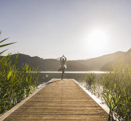 Woman practicing tree pose on jetty by lake - UUF27418