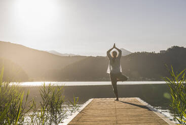 Mature woman doing tree pose on jetty by lake at vacation - UUF27419