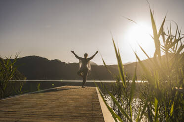 Woman balancing with arms raised on jetty by mountains - UUF27420