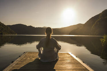 Woman meditating on jetty over lake at vacation - UUF27426