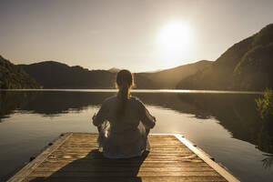 Woman meditating on jetty over lake at vacation - UUF27426