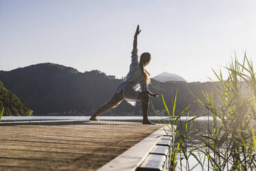 Mature woman doing yoga on jetty by lake - UUF27430