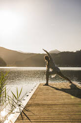 Ältere Frau übt Yoga auf Steg über See im Urlaub - UUF27431