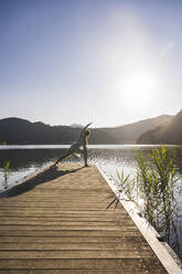 Woman stretching on jetty over lake by mountains - UUF27432