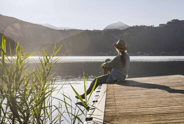 Reife Frau mit Hut schaut auf den See vom Steg im Urlaub - UUF27438