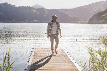 Mature man in plaid shirt walking on jetty at vacation - UUF27461