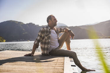 Thoughtful man sitting on jetty over lake - UUF27463