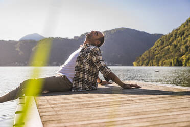 Älterer Mann entspannt sich mit geschlossenen Augen auf einem Steg über einem See - UUF27465