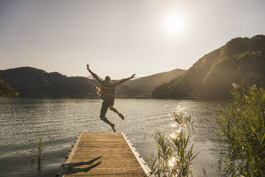 Mature man jumping with arms raised on jetty - UUF27469