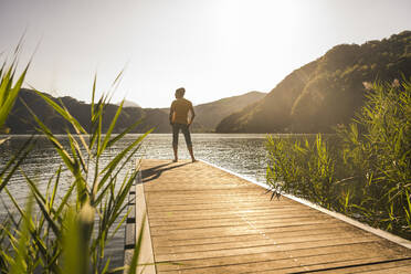 Man standing on jetty over lake by mountains at vacation - UUF27472