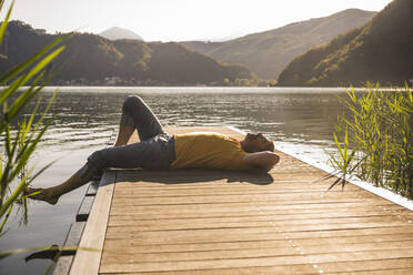 Älterer Mann entspannt sich auf einem Steg über einem See in den Bergen - UUF27477