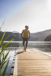 Mature man walking with hands in pockets on jetty at vacation - UUF27478