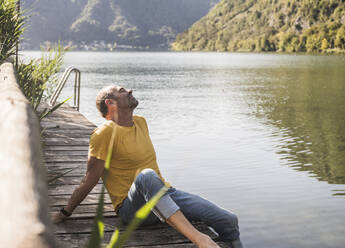 Man relaxing with eyes closed on jetty by lake - UUF27484