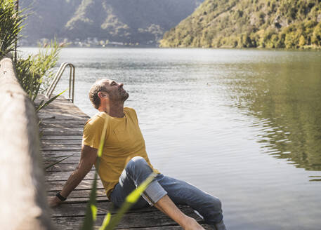 Mann entspannt sich mit geschlossenen Augen auf einem Steg am See - UUF27484