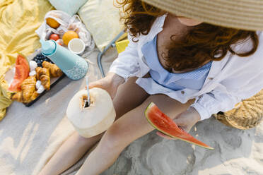 Frau mit Kokosnuss und Scheibe Wassermelone am Strand sitzend - TYF00439