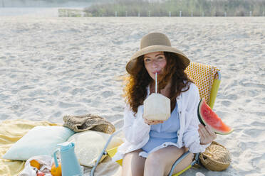 Frau mit Hut trinkt Kokosnusswasser am Strand - TYF00440