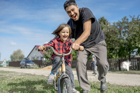 Fröhlicher Vater bringt glücklichem Sohn an einem sonnigen Tag das Fahrradfahren bei - ANAF00094