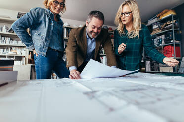 Planer arbeiten im Büro an der Fertigstellung eines Wohnungsbauplans, Architekten sehen sich Baupläne an. - JLPSF02448