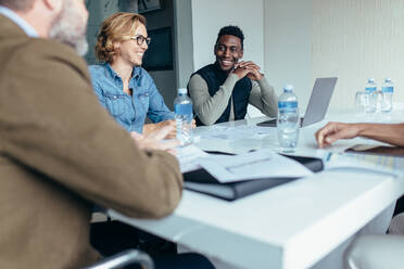 Lächelnde Geschäftsfrau in einer Besprechung mit Kollegen im Konferenzraum. Weibliche Führungskraft leitet Brainstorming-Sitzung im Designbüro. - JLPSF02449