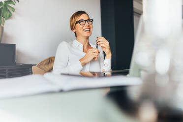 Smiling business woman in spectacles sitting at her desk in office. Woman sitting in office holding a pen in a happy mood. - JLPSF02457