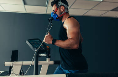 Sportsman with mask running on treadmill. Male athlete in sports science lab measuring his performance and oxygen consumption. - JLPSF02460