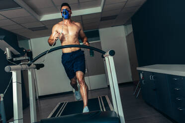 Männlicher Sportler bei der Überprüfung seiner Fitness im Sportlabor. Läufer mit Maske bei einem Leistungstest auf dem Laufband. - JLPSF02464