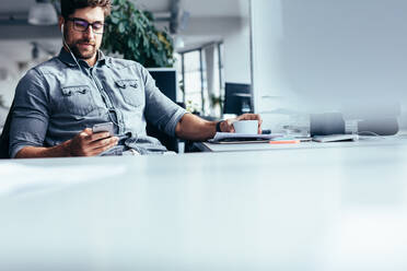 Young businessman using smart phone at his work place. Caucasian young man listening music from his mobile phone. - JLPSF02471