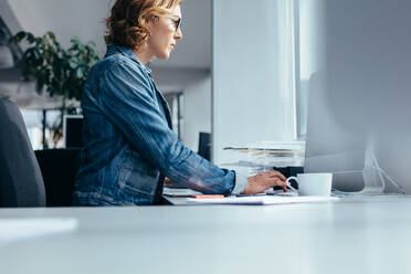 Seitenansicht einer jungen Geschäftsfrau, die im Büro arbeitet. Eine Designerin sitzt und benutzt einen Laptop. - JLPSF02472