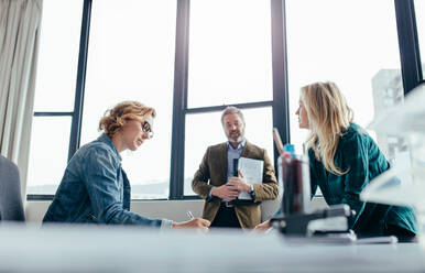 Geschäftsleute arbeiten in einem modernen Büro, eine Geschäftsfrau sitzt an ihrem Schreibtisch, ihre Kollegen stehen daneben. - JLPSF02481