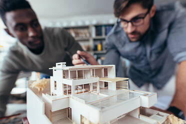 Close up shot of scale model house on table with architects. Two architects making architectural model in office together. - JLPSF02486