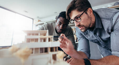 Zwei männliche Architekten im Büro diskutieren über ein Hausmodell. Architekt arbeitet an einem Architekturmodell. - JLPSF02487