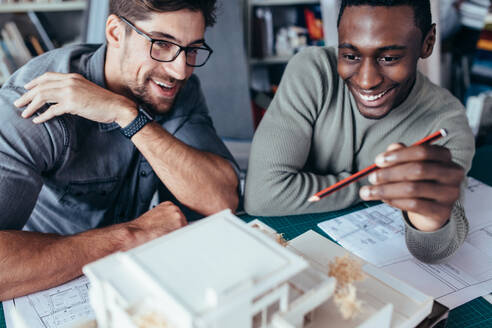 Zwei Mitarbeiter besprechen ein Wohnungsmodell im Büro. Architekten arbeiten an einem Gebäudemodell. - JLPSF02495