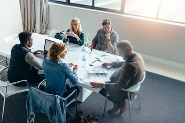 Business people working and discussing together in meeting at office. Businessman looking at building sketch with colleagues sitting around table. - JLPSF02524