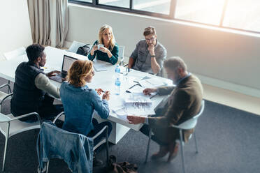 Geschäftsleute arbeiten und diskutieren zusammen in einem Meeting im Büro. Geschäftsmann schaut auf eine Gebäudeskizze mit Kollegen, die am Tisch sitzen. - JLPSF02524