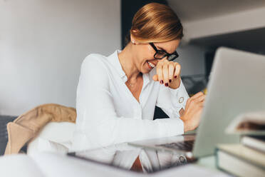 Business woman in spectacles sitting at her desk in office and laughing. Woman sitting in office with laptop computer on her desk. - JLPSF02579