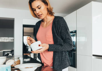 Frau, die in ihrer Küche ein gesundes Frühstück zubereitet. Frau, die ihren Haferflocken etwas hinzufügt. - JLPSF02585