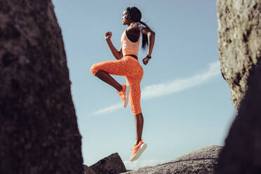 Afrikanische Athletin, die im Freien über Felsen springt und sich dehnt. Gesunde und starke Frau beim Training. - JLPSF02605