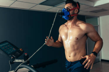 Fit and muscular athlete with mask running on treadmill for monitoring his performance. Sportsman in sports science lab measuring his performance. - JLPSF02629