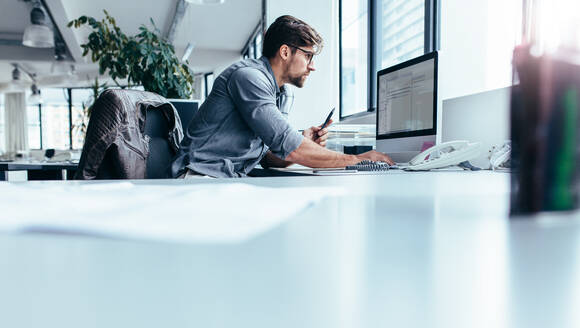 Junger Mann sitzt im Büro und arbeitet am Desktop-PC. Geschäftsmann schaut auf Computer-Monitor bei der Arbeit im Büro. - JLPSF02642