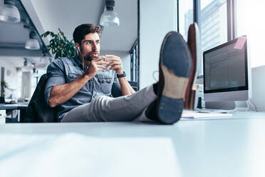 Male designer listening music with cup of coffee. Young man drinking coffee during break in office. - JLPSF02654