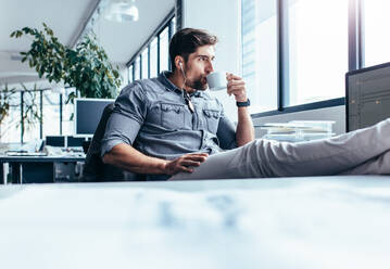 Junger Mann trinkt Kaffee während der Pause im Büro. Geschäftsmann hört Musik mit einer Tasse Kaffee. - JLPSF02655