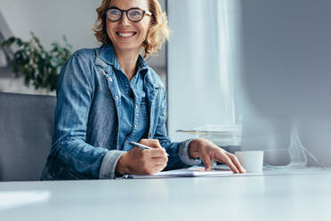 Schöne junge Geschäftsfrau sitzt im Büro, schaut weg und lächelt. Weibliche Führungskraft bei der Arbeit. - JLPSF02659