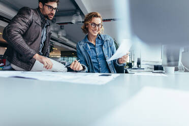 Zwei Architekten arbeiten an einem Bauplan in einem Büro. Glückliche Geschäftspartner arbeiten zusammen am Schreibtisch. - JLPSF02668