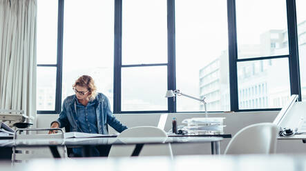 Young businesswoman working at her desk. Female designer working on blueprint in office. - JLPSF02677