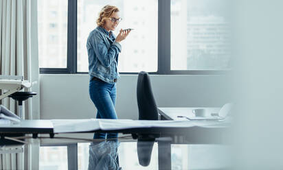 Horizontale Aufnahme einer Geschäftsfrau, die im Büro ein Mobiltelefon benutzt. Eine Architektin spricht über einen Lautsprecher. - JLPSF02686